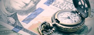 A pocketwatch sitting on top of a one hundred dollar bill