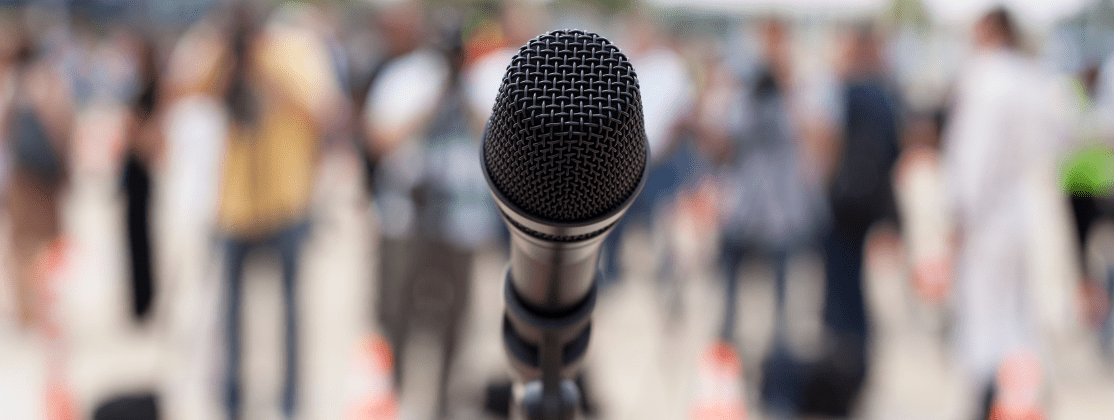A microphone on a stand with a crowd of people blurred in the background.