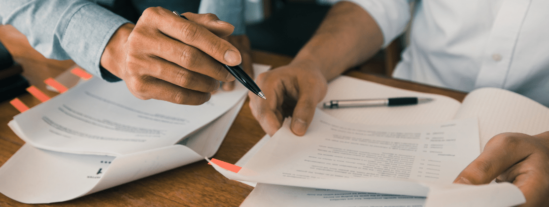 Two people looking over papers at a desk with pens in hand.